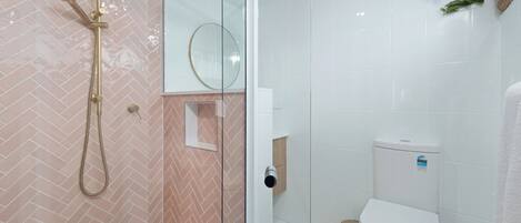 A modern bathroom with a glass shower enclosure, a white toilet, and a herringbone-patterned wall.
