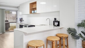 Une cuisine moderne avec des meubles blancs, un îlot central intégré doté de tabourets et une machine à café.