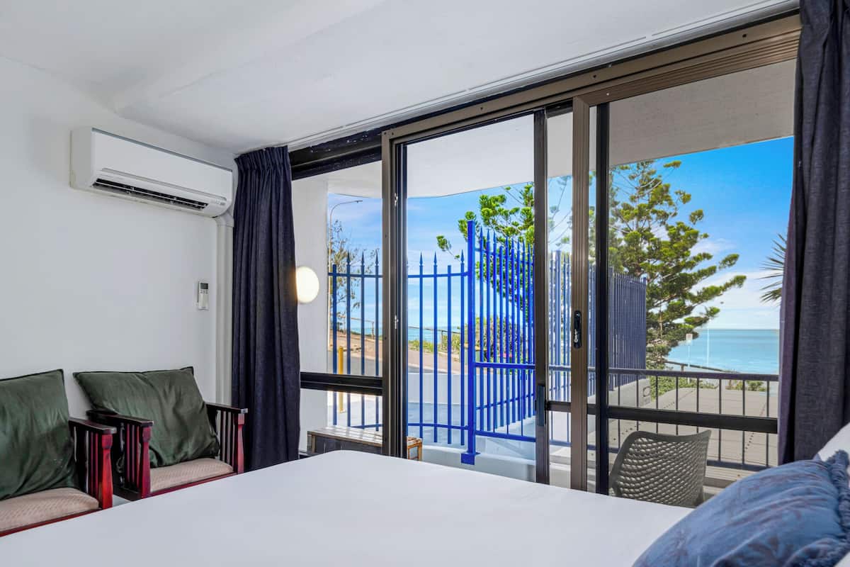 Una habitación de hotel con cama, sofá, ventana y vista al mar, además de una valla azul.