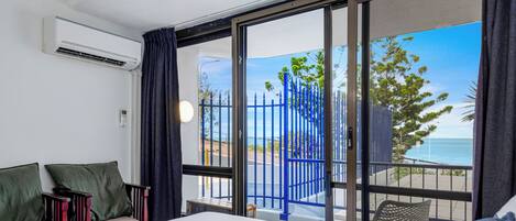 A hotel room with a bed, a sofa, a window with a view of the sea and a blue fence.