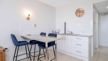 Une cuisine moderne avec un coin repas, dotée d’un plan de travail en granit, de meubles blancs et de tabourets de bar bleus.