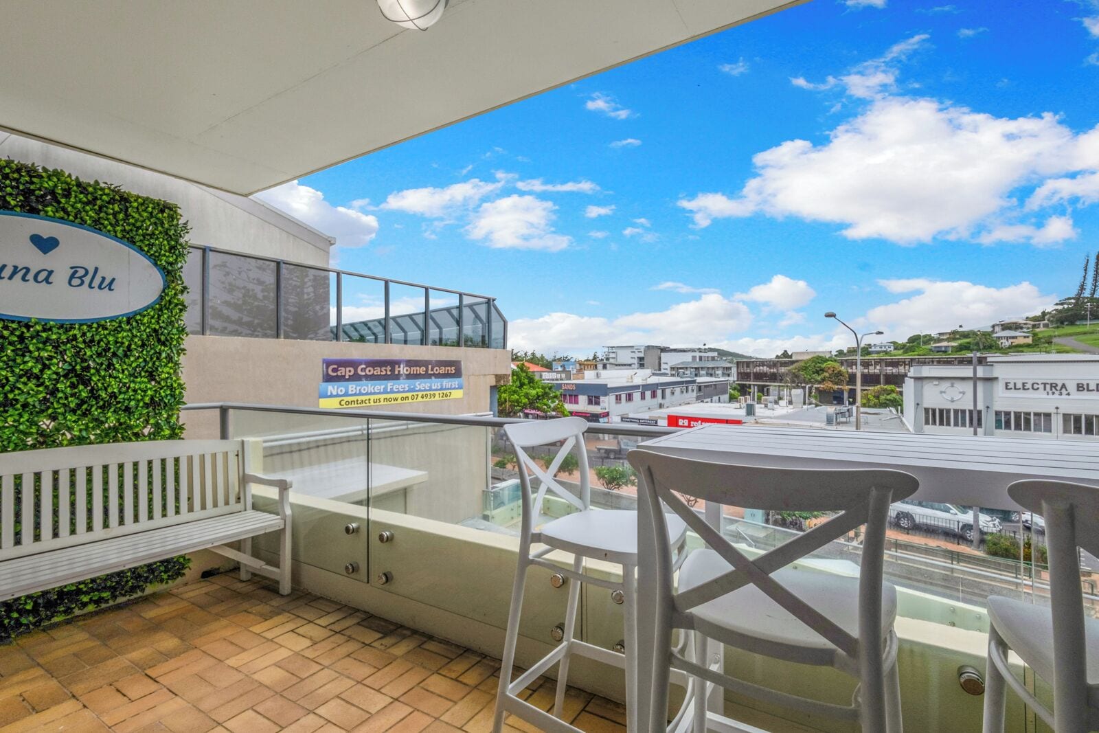 A balcony with a view of the city, a sign for Cap Coast Home Loans, and a bench.
