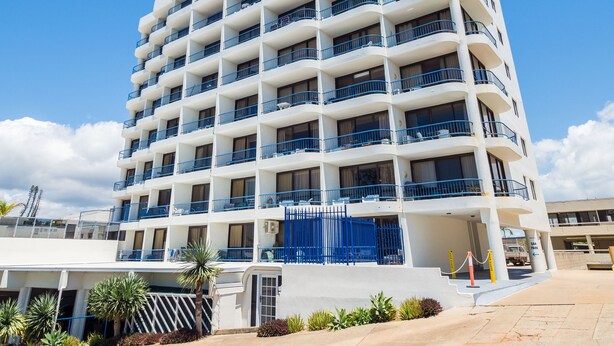 A multi-story hotel with balconies, a clear sky, and a parking area.