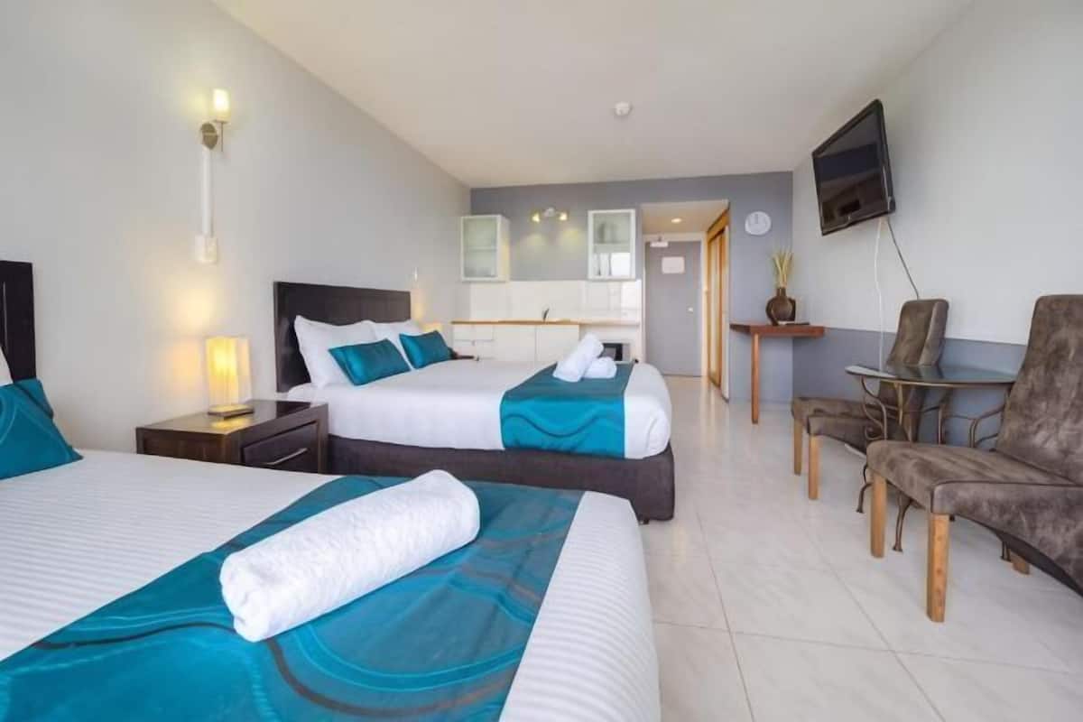 Una habitación de hotel con dos camas, televisión, una mesita y un rincón de descanso.