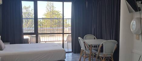 A hotel room with a bed, a dining table with chairs, a ceiling-mounted security camera, and a view of the outdoors.
