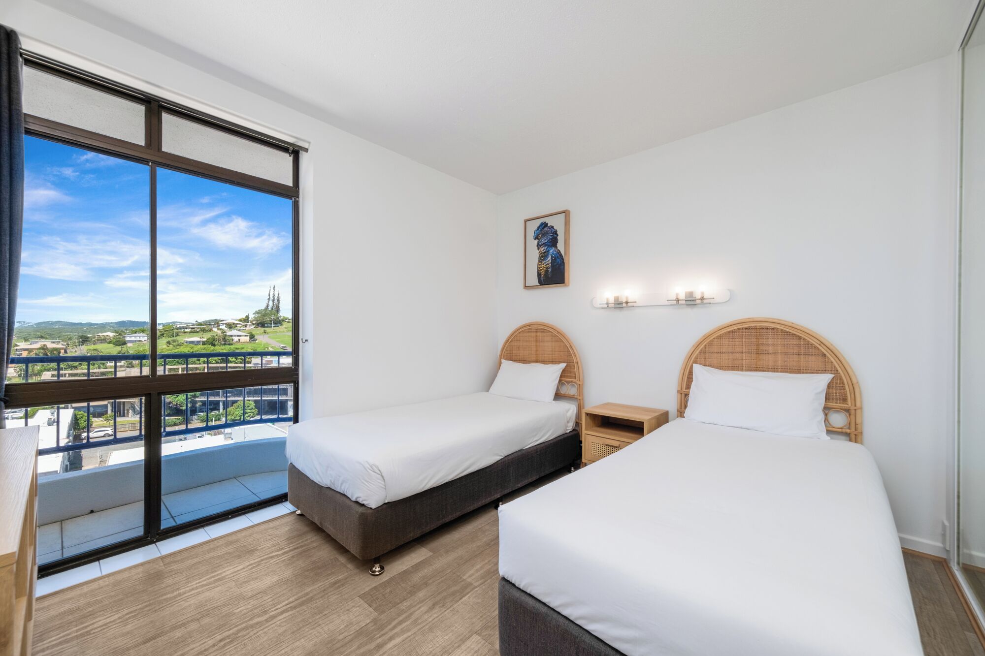 Hotelkamer met twee bedden, een groot raam met uitzicht, een wandlamp en een lijst met een afbeelding.