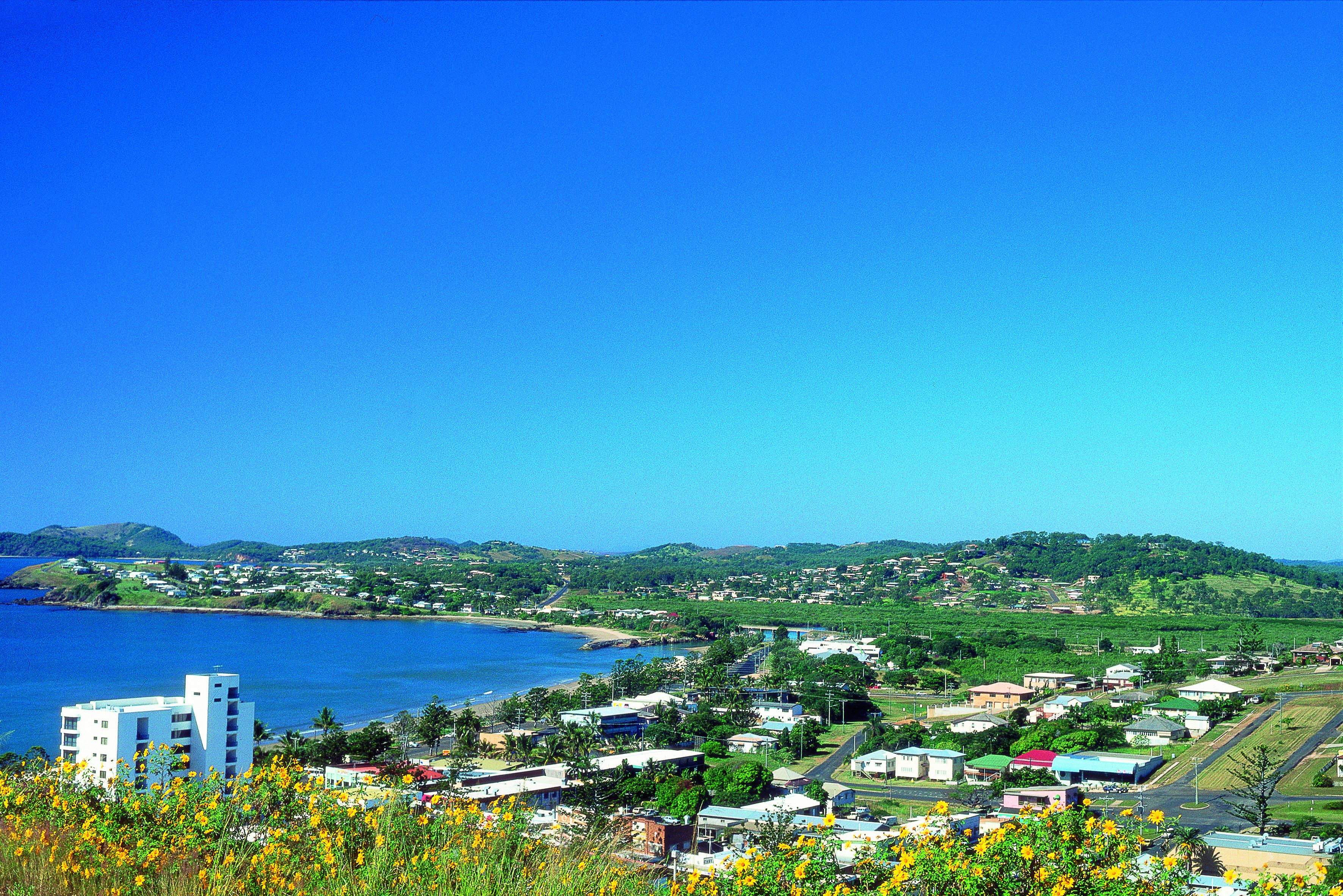 A coastal town with buildings, a beach, and hills in the background.