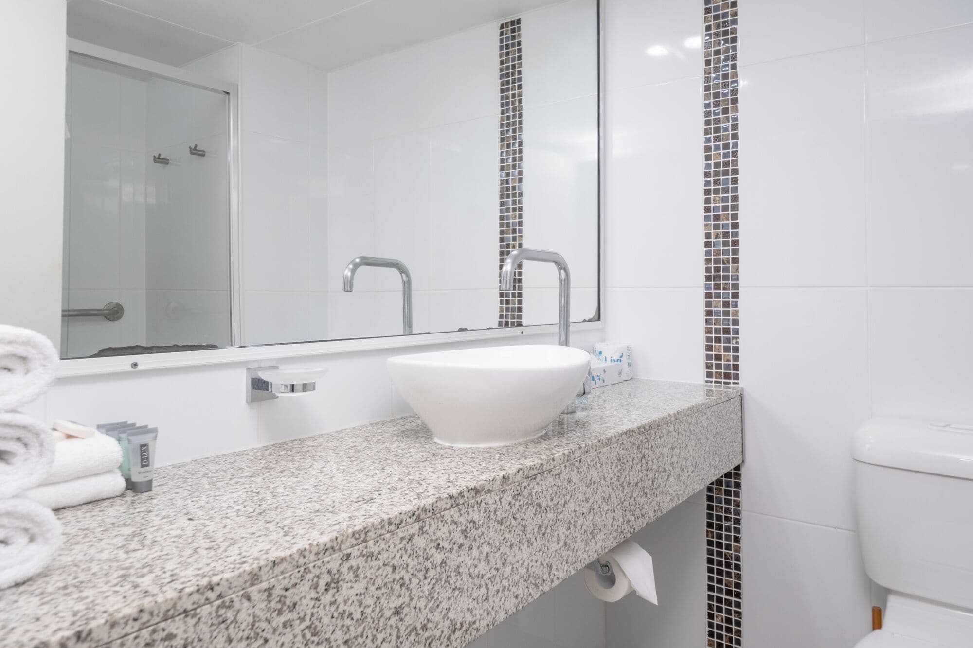 Un baño con un lavamanos blanco, un espejo, una ducha e inodoro.