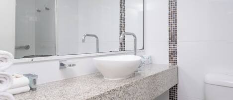 Un baño con un lavamanos blanco, un espejo, una ducha e inodoro.