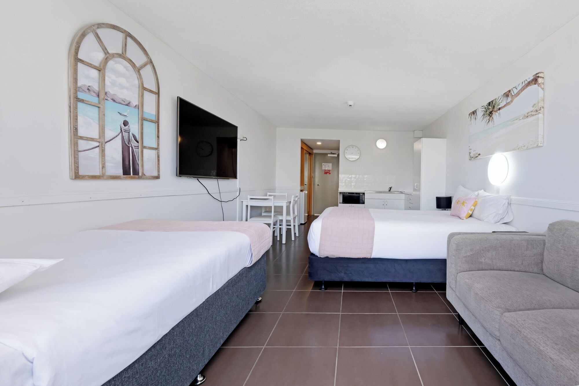Quarto de hotel com duas camas, televisão, secretária e cozinha compacta.