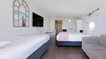 Quarto de hotel com duas camas, televisão, secretária e cozinha compacta.