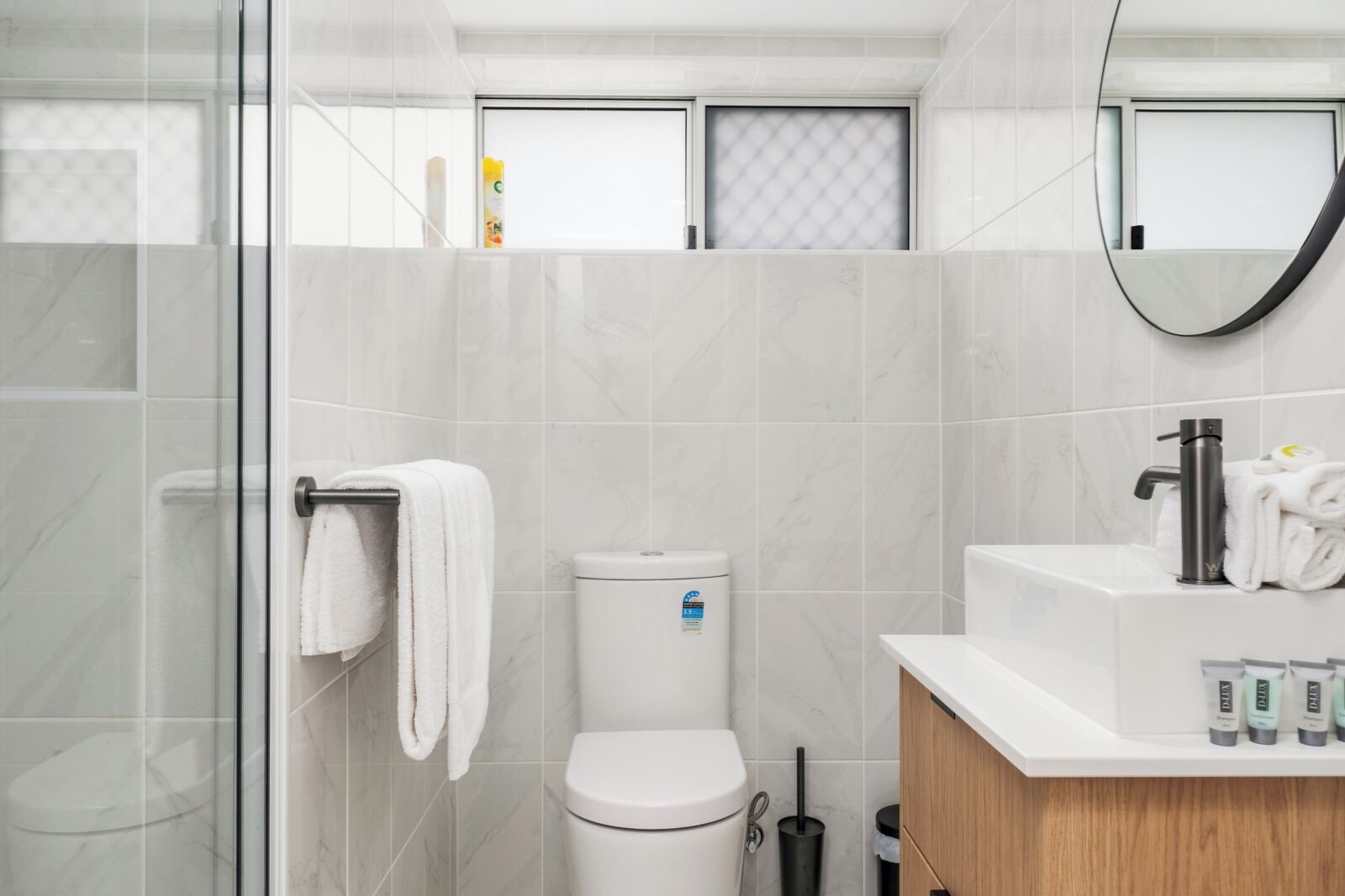 A modern bathroom with a glass shower enclosure, a white toilet, and a vanity with toiletries.