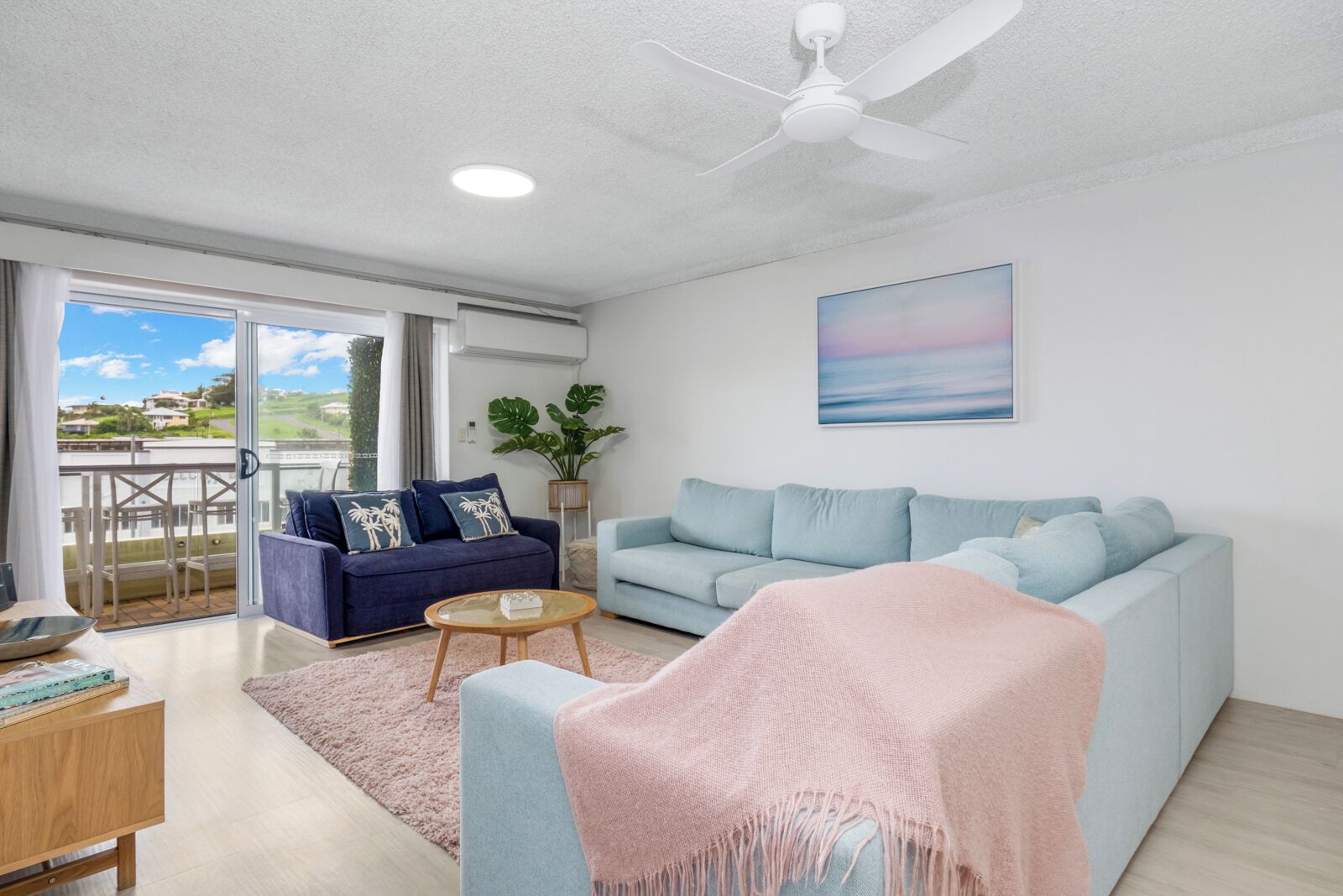 A modern living room with a sofa, a coffee table, and a balcony with a view.