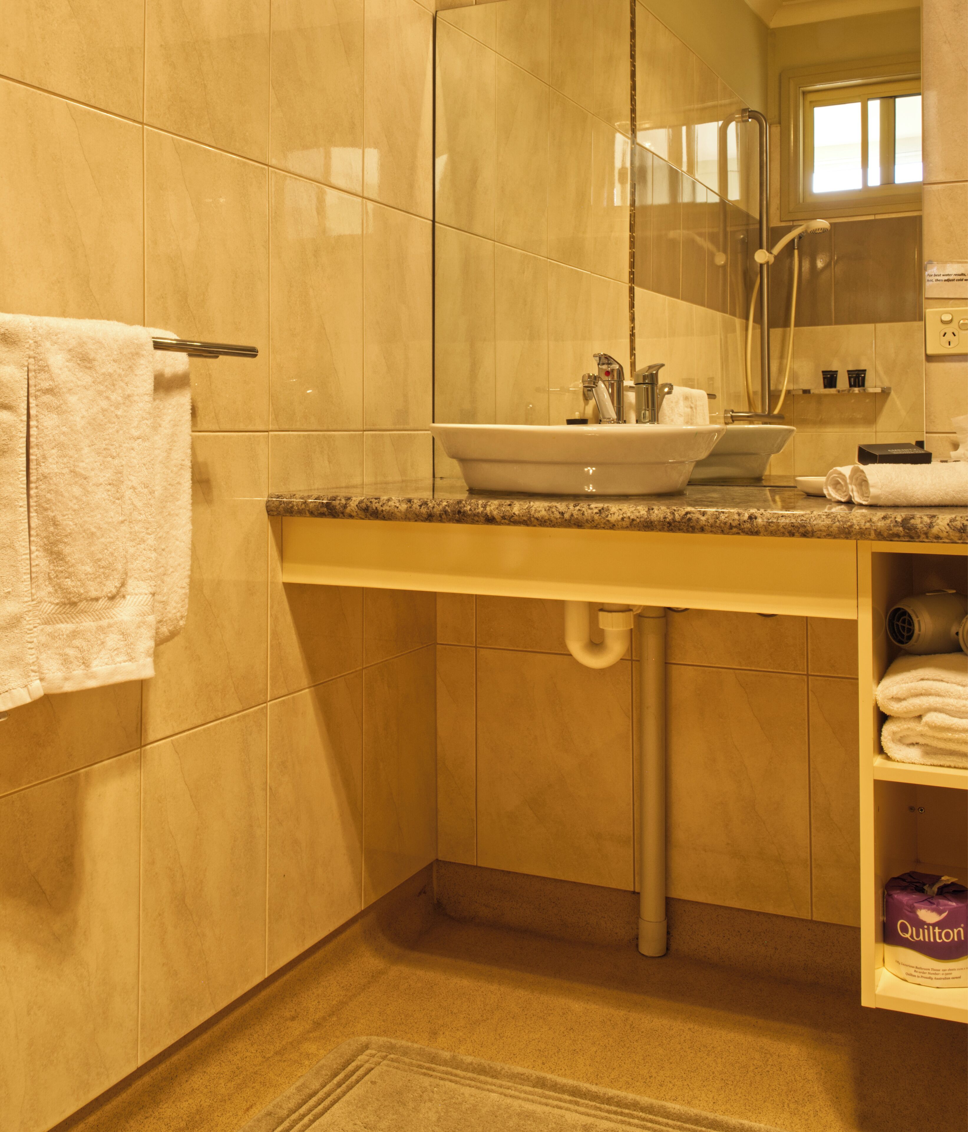Un baño con lavamanos, espejo, toallero y repisas con artículos de aseo.
