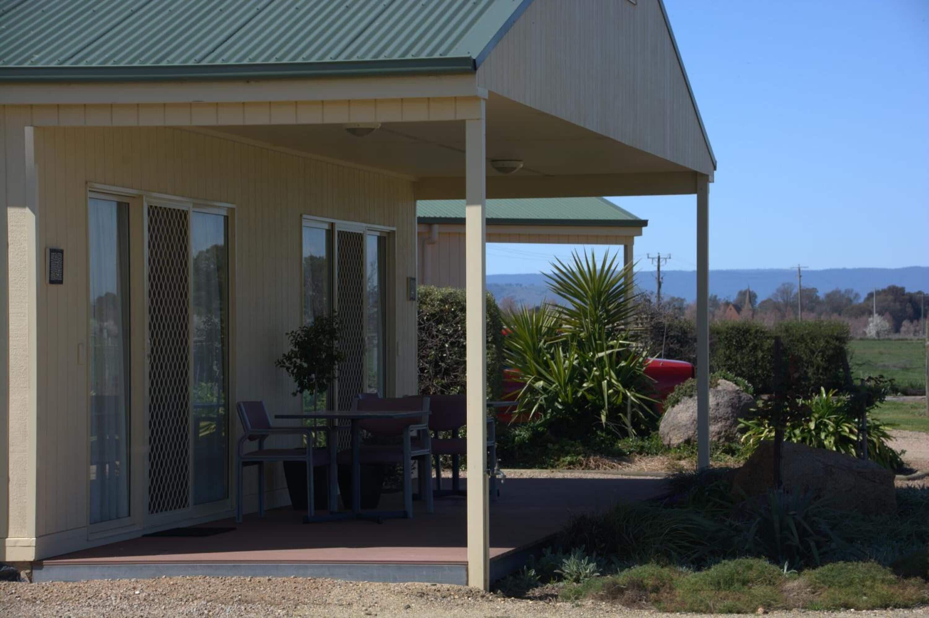 A covered outdoor area with a table and chairs, a view of the landscape, and a building with a green roof.