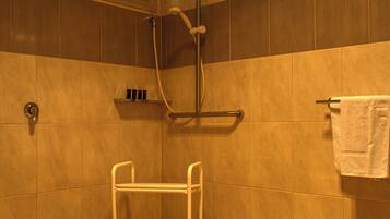 Zona doccia con sedia per disabili, porta asciugamani e finestra sopra la doccia.