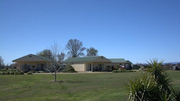 A two-story building with a green roof, surrounded by a grassy lawn and a few trees.