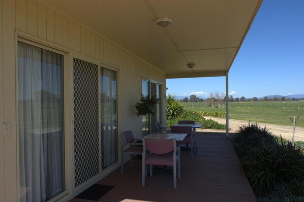 A covered patio with a table and chairs, sliding glass doors, and a view of a green landscape. - Milawa Muscat Retreat B&B (Milawa)