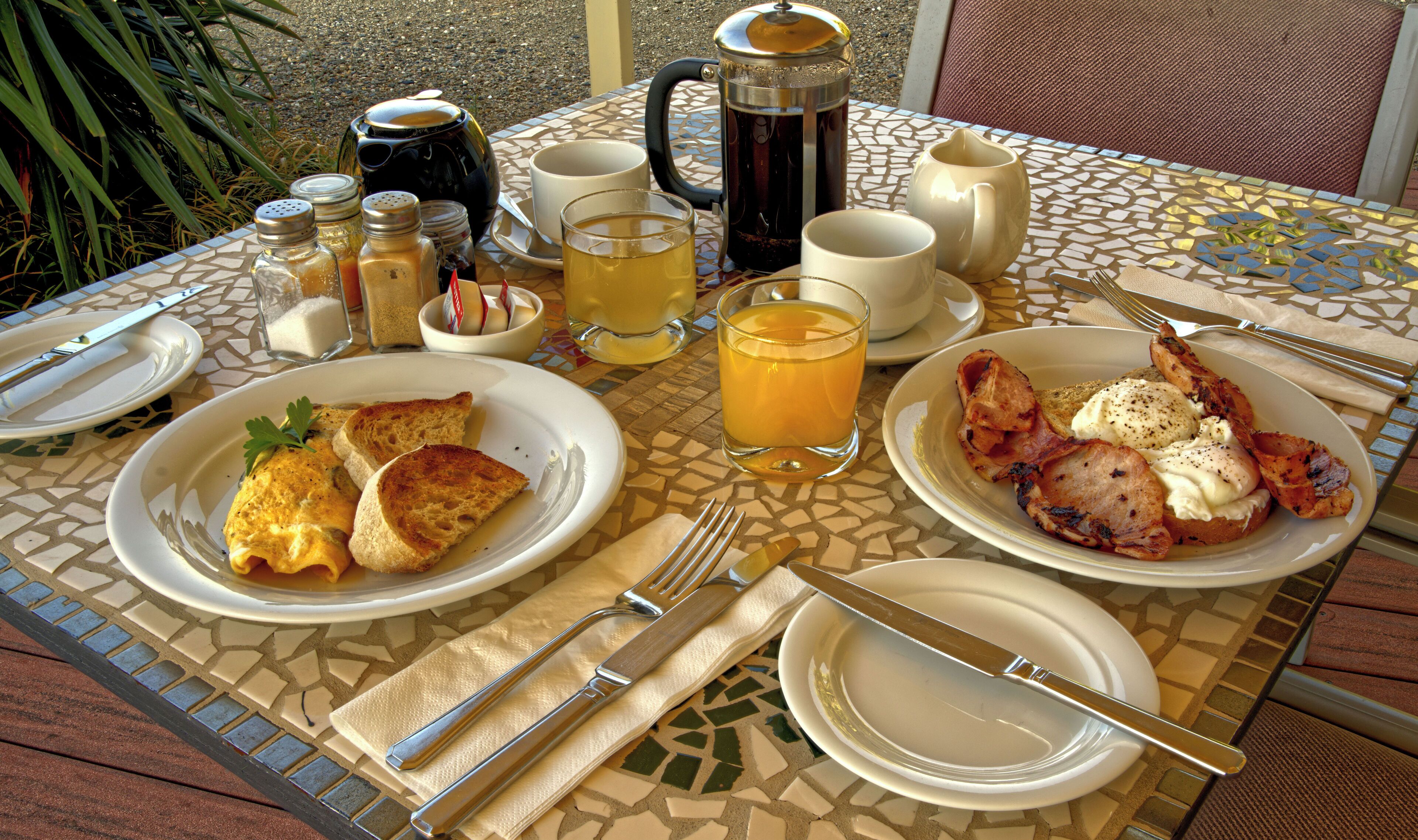 A breakfast table with plates of food, a coffee pot, and various condiments.