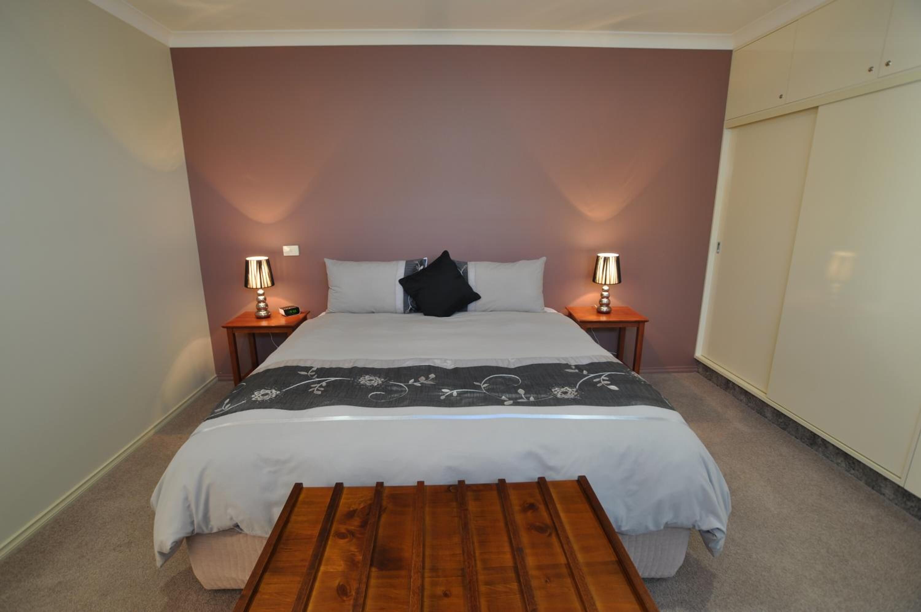 A bedroom with a bed, bedside tables, a bench, and a wardrobe.
