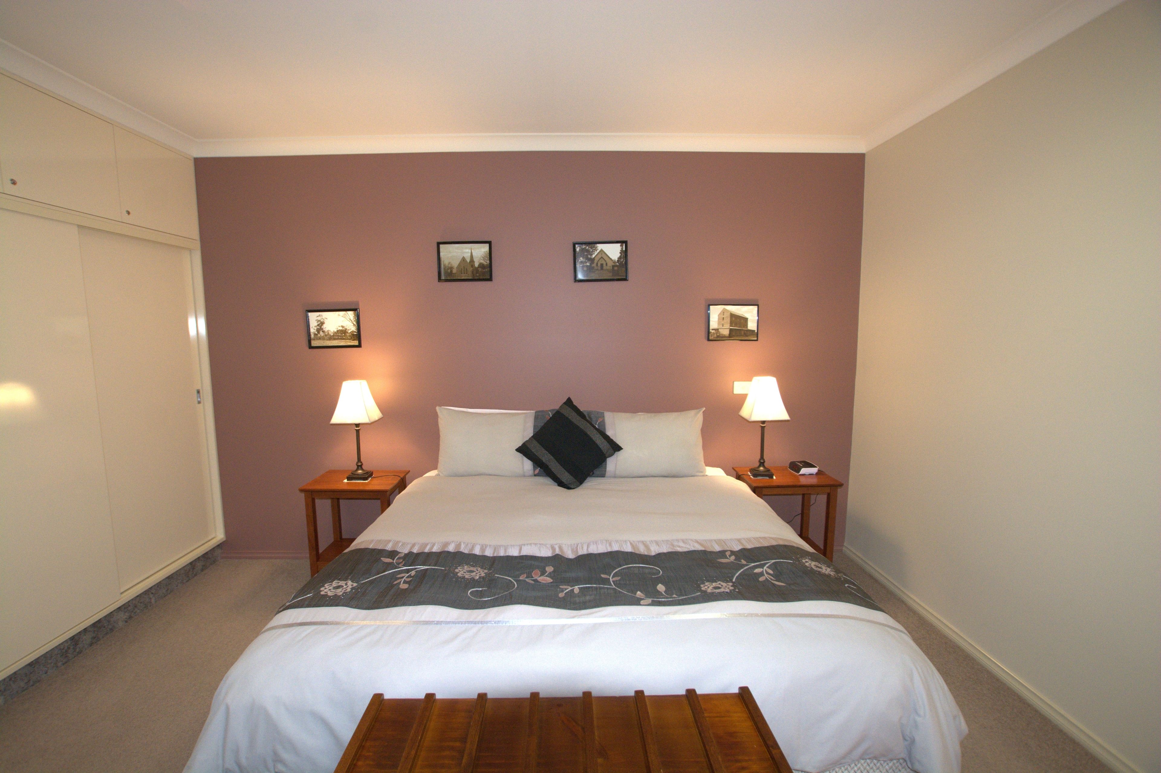 Un lit bien fait, recouvert d’une couvre-lit à motifs floraux, avec deux lampes de chevet et trois tableaux encadrés accrochés au mur.