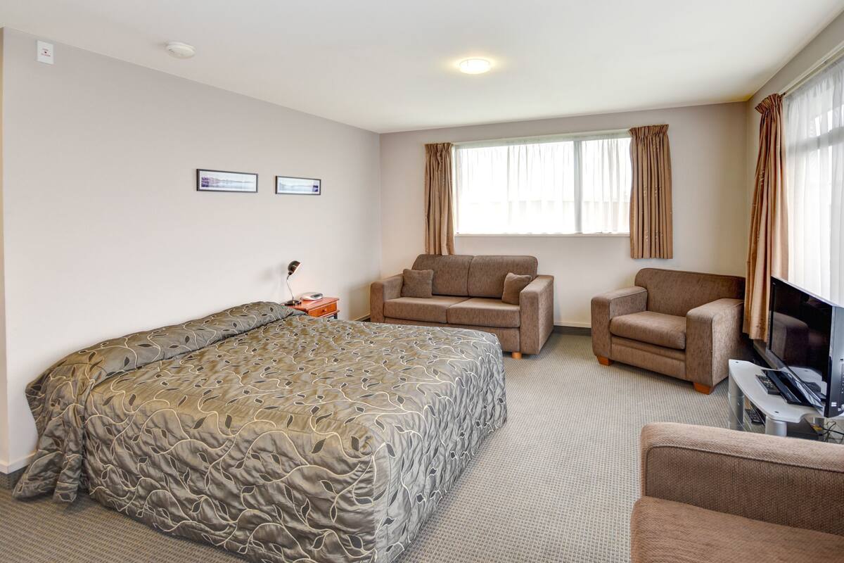 A hotel room with a large bed, two armchairs, a TV, and a window with curtains.