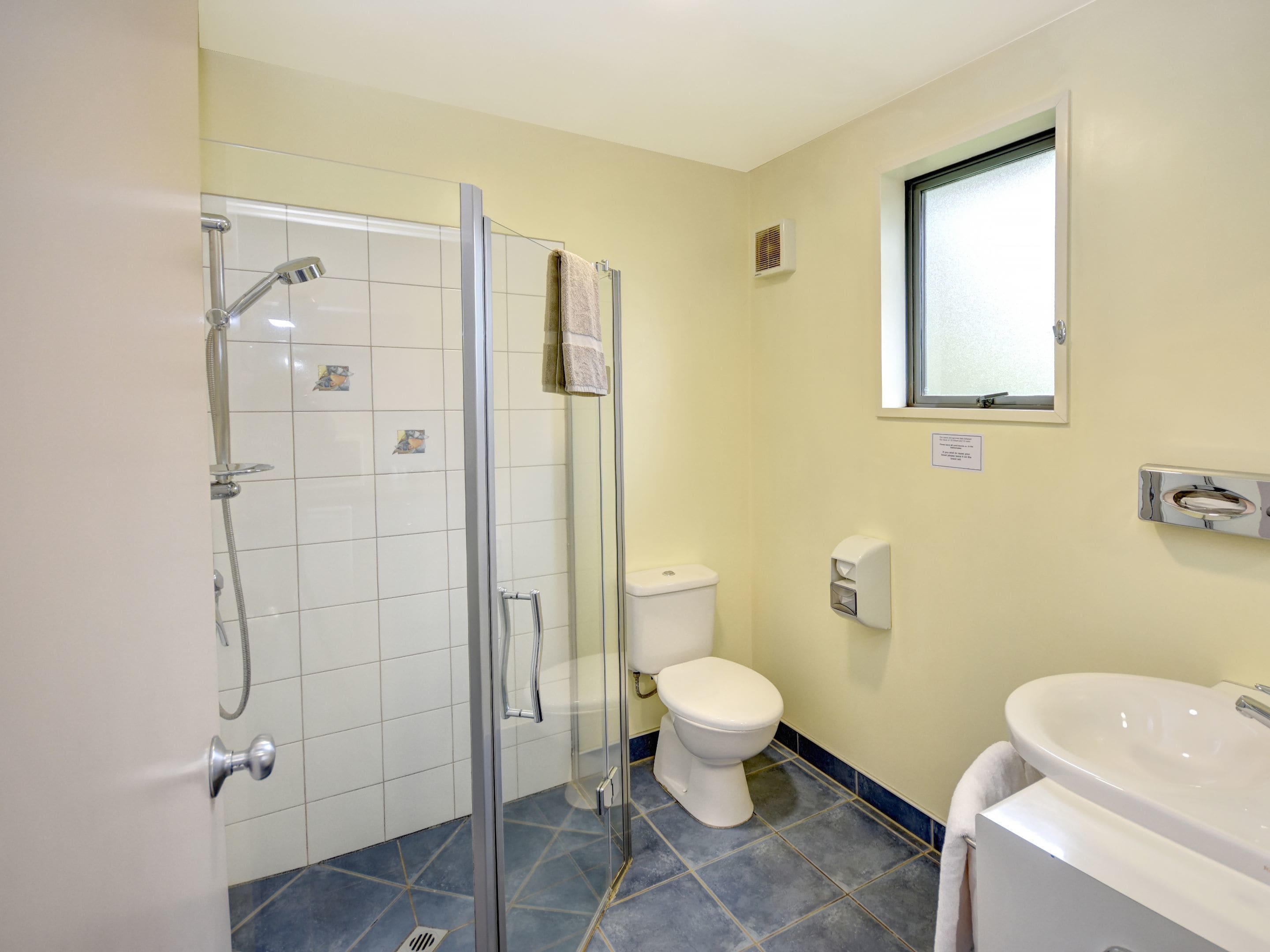 A bathroom with a glass shower enclosure, a white toilet, and a white sink.