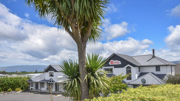 A motel with a sign, surrounded by greenery and a clear sky. - Bonnie Knights Motel (Mosgiel)