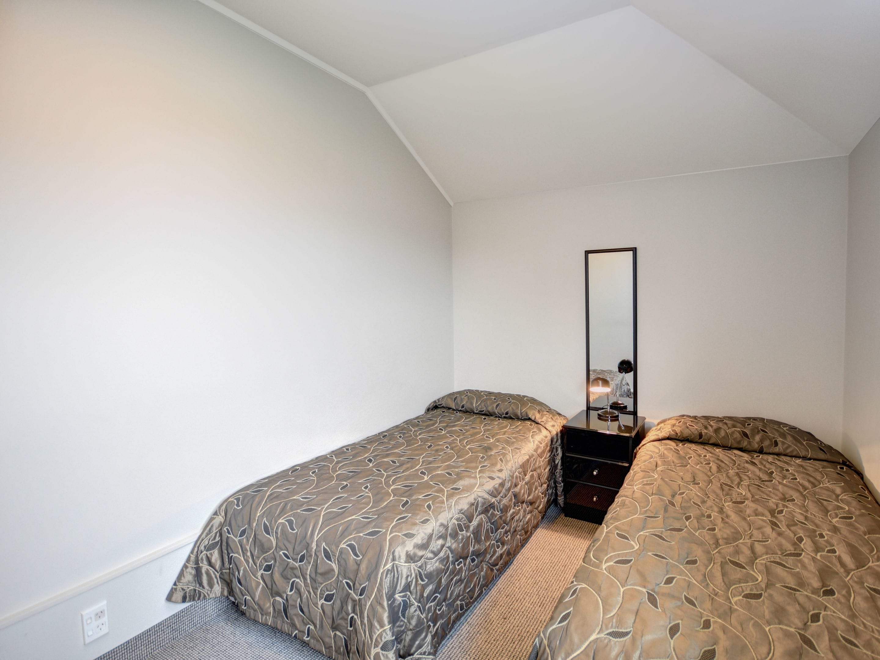 A bedroom with two single beds, a nightstand, a mirror, and a wall socket.