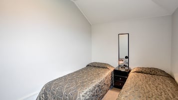 A bedroom with two single beds, a nightstand, a mirror, and a wall socket.