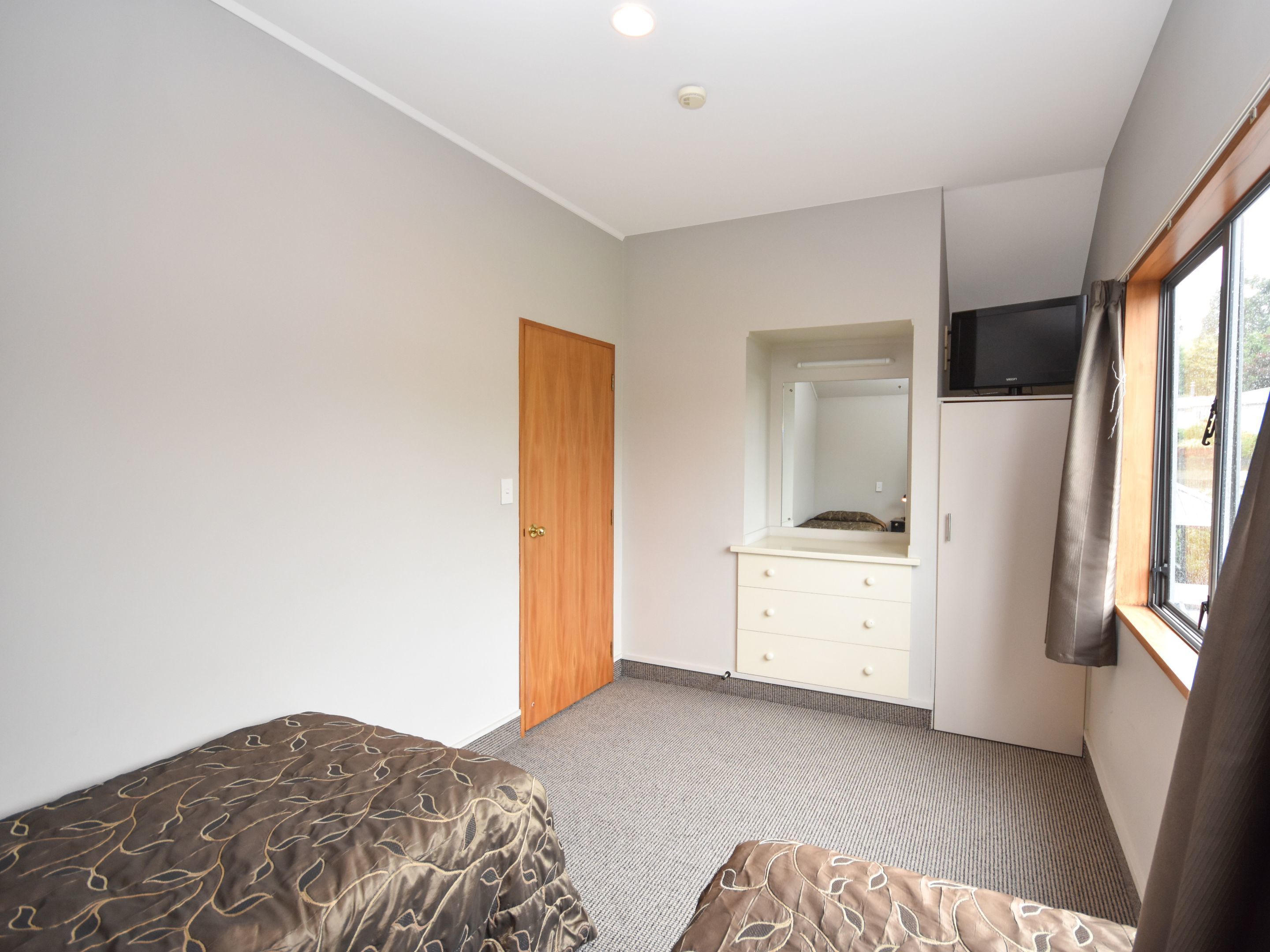 A bedroom with a bed, a dresser, a mirror, and a window.
