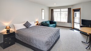 A hotel room with a large bed, a desk, a chair, a TV, and a window with curtains. - Bonnie Knights Motel (Mosgiel)