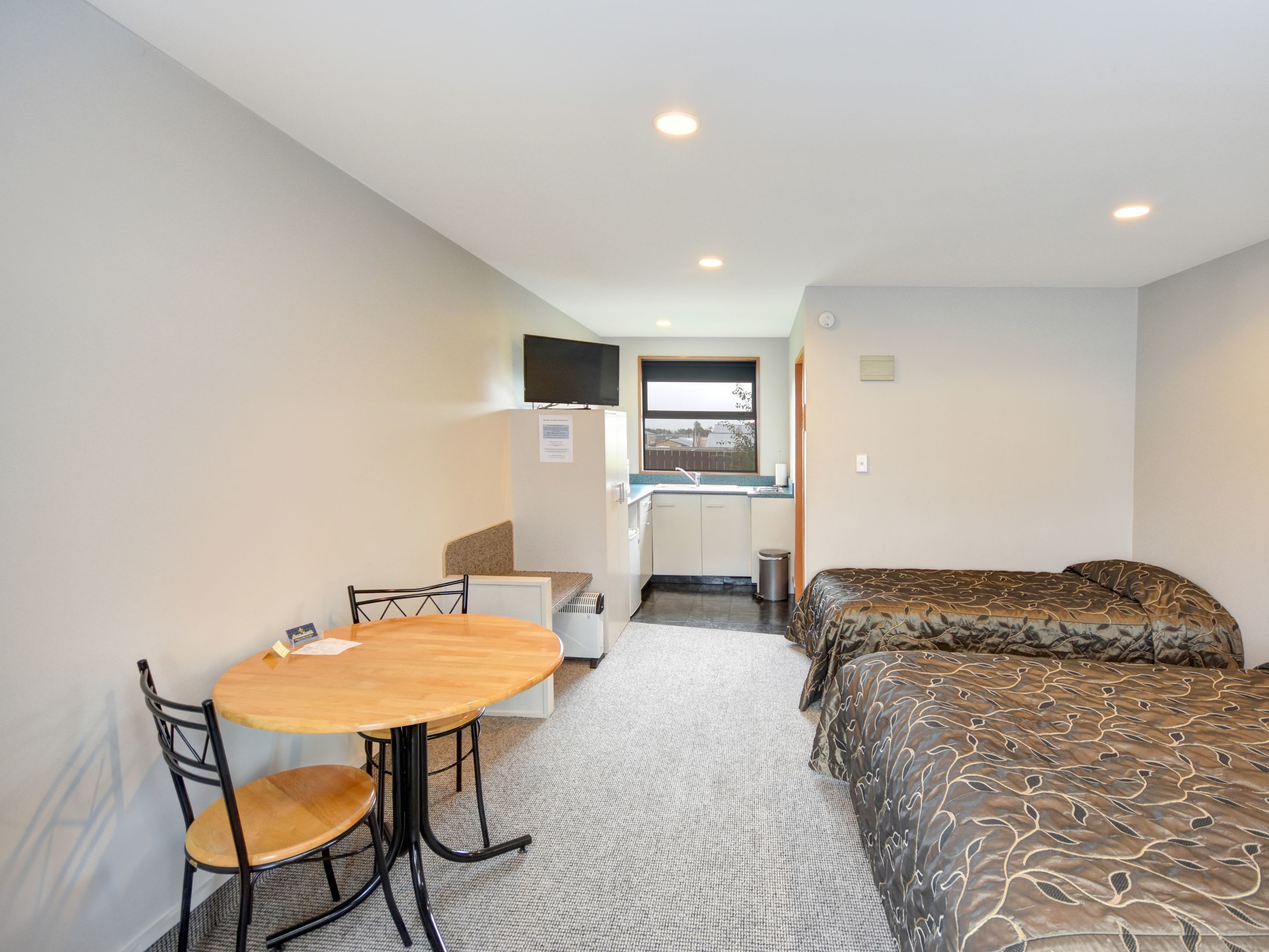 Una habitación compacta con cama, una kitchenette pequeña, una mesa de comedor con sillas y un televisor montado en la pared.