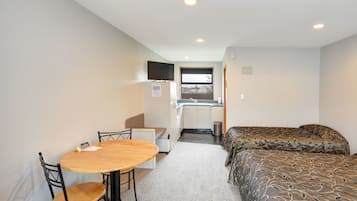 Una habitación compacta con cama, una kitchenette pequeña, una mesa de comedor con sillas y un televisor montado en la pared.