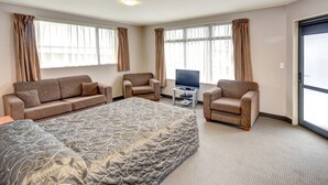 A hotel room with a large bed, two armchairs, a TV on a stand, and a sliding glass door. - Bonnie Knights Motel (Mosgiel)