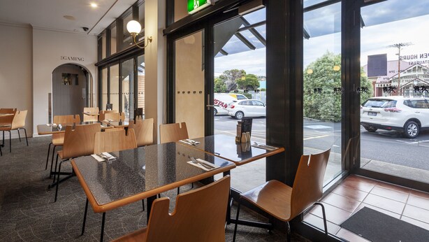 A restaurant with a modern interior, featuring a glass partition with a view of the street, a green exit sign, and a menu stand. - Black Buffalo Hotel (North Hobart)