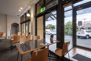 Ein Restaurant mit modernem Interieur, das eine Glastrennwand mit Blick auf die Straße, ein grünes Fluchtzeichen und einen Menüständer zeigt.