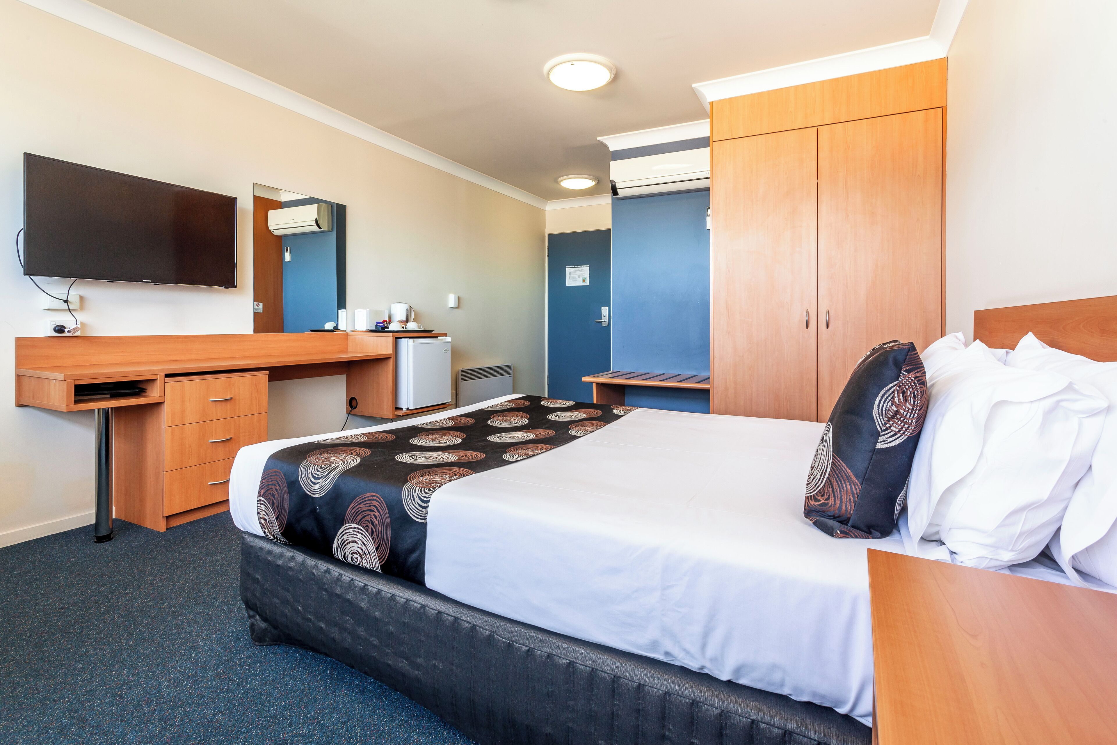 A hotel room with a bed, a desk, a television, and a wardrobe.