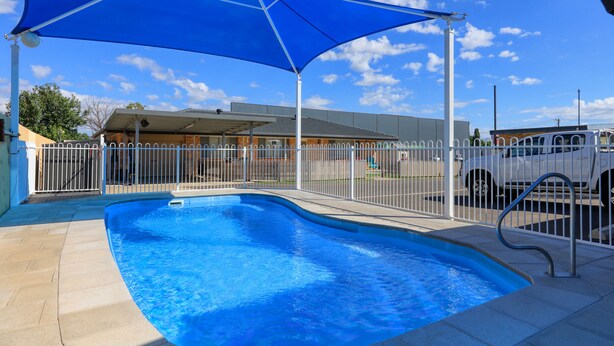 A swimming pool with a blue shade sail, a white fence, and a metal ladder.