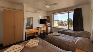 A hotel room with two beds, a desk, a television, and a window with a view of houses.