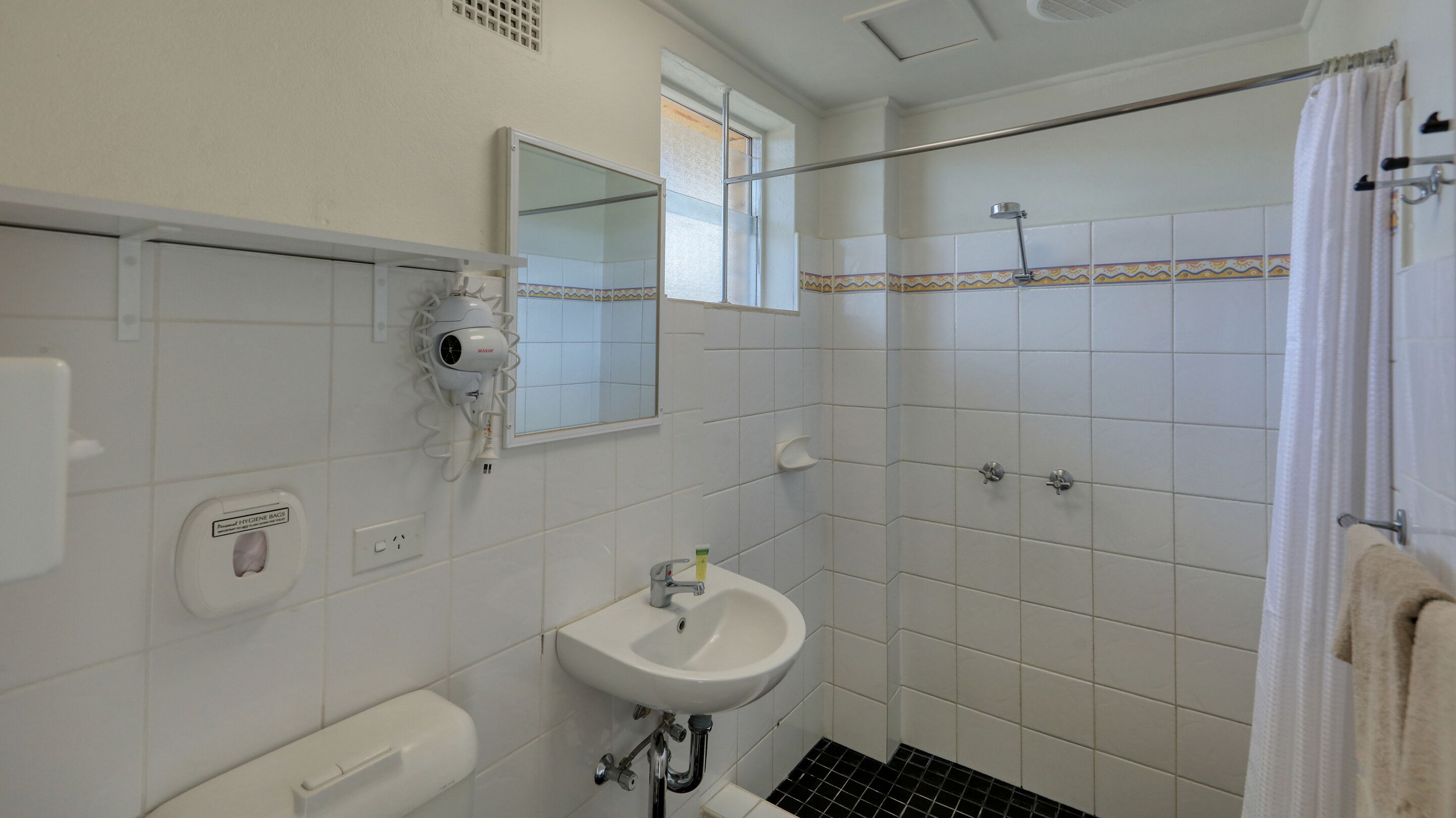 Une salle de bain avec un lavabo blanc, un miroir, un sèche-cheveux et un espace douche.