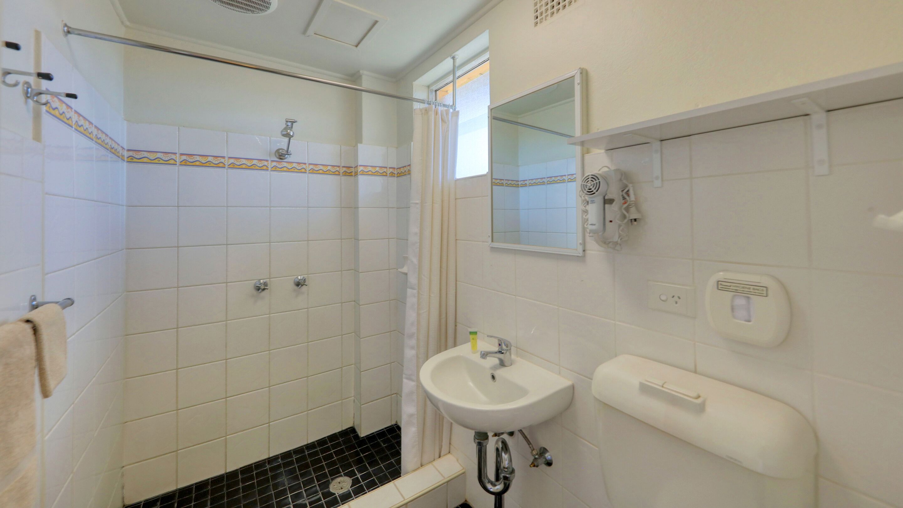 A bathroom with white tiled walls, a shower, a sink, and a toilet.