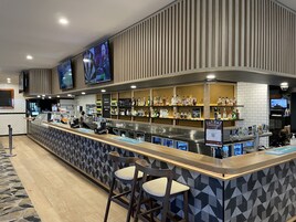 Un área de bar moderna con mostrador, taburetes y estantes llenos de botellas de licores.