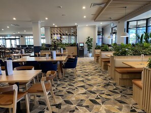 Un espace repas moderne doté de plusieurs tables et de banquettes, d’un sol à motifs et de grandes fenêtres laissant entrer la lumière naturelle.