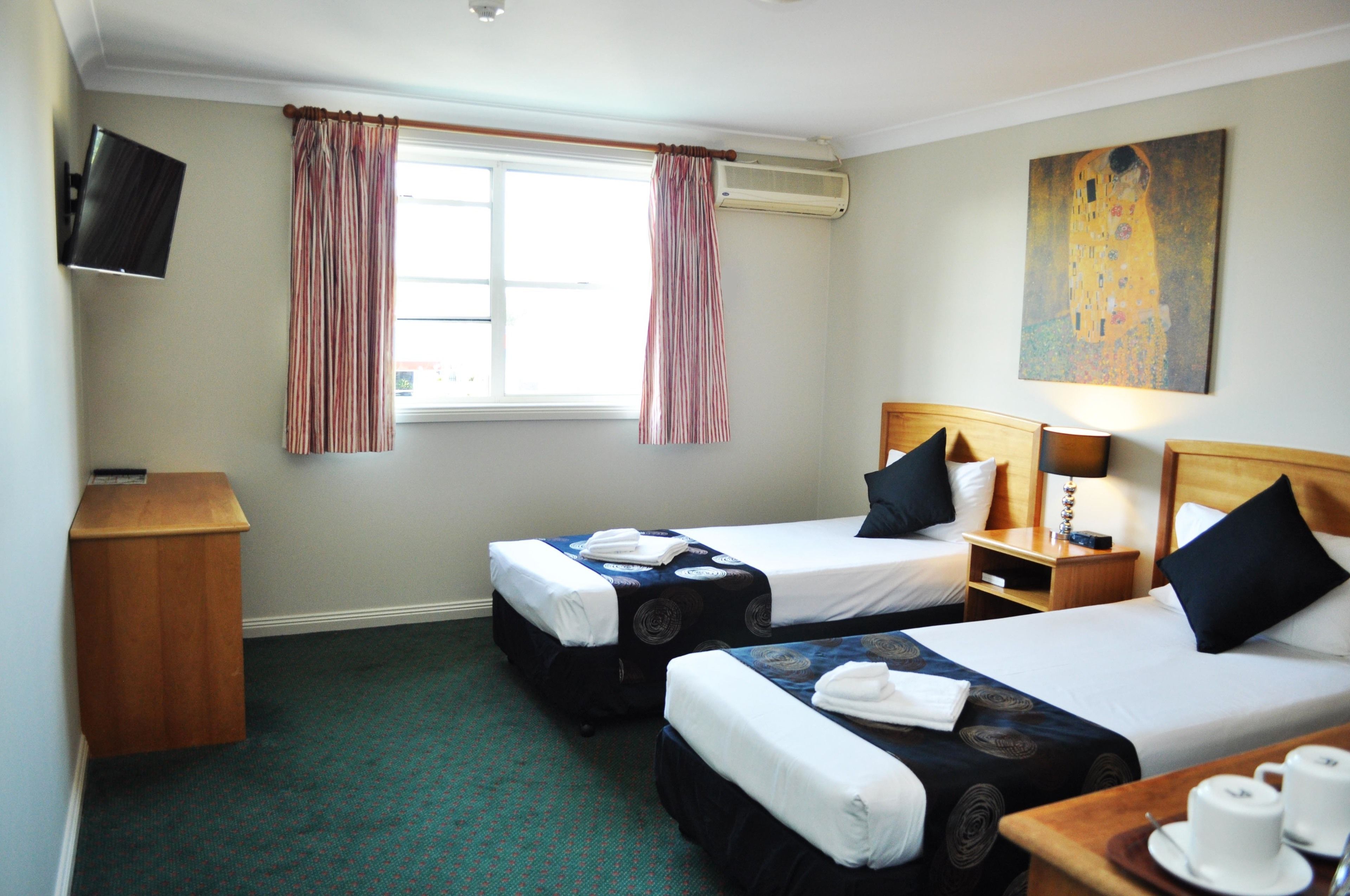 A hotel room with two single beds, a TV, a painting, and a window with curtains.