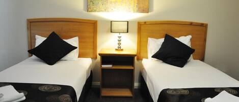 Habitación de hotel con dos camas individuales, una mesita de noche con lámpara y un cuadro sobre las camas.