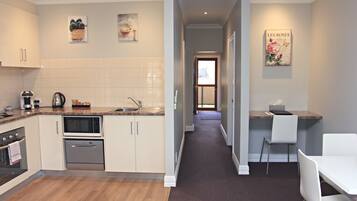 A modern kitchen with white cabinets, a microwave, and a sink. There is a hallway leading to a dining area with a table and chairs.