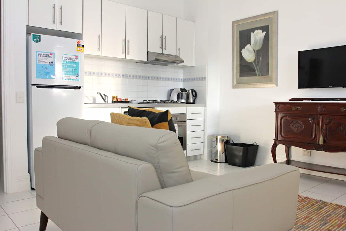 Una cocina moderna con armarios blancos, un refrigerador y una estufa. Hay un sofá en primer plano y un televisor montado en la pared.