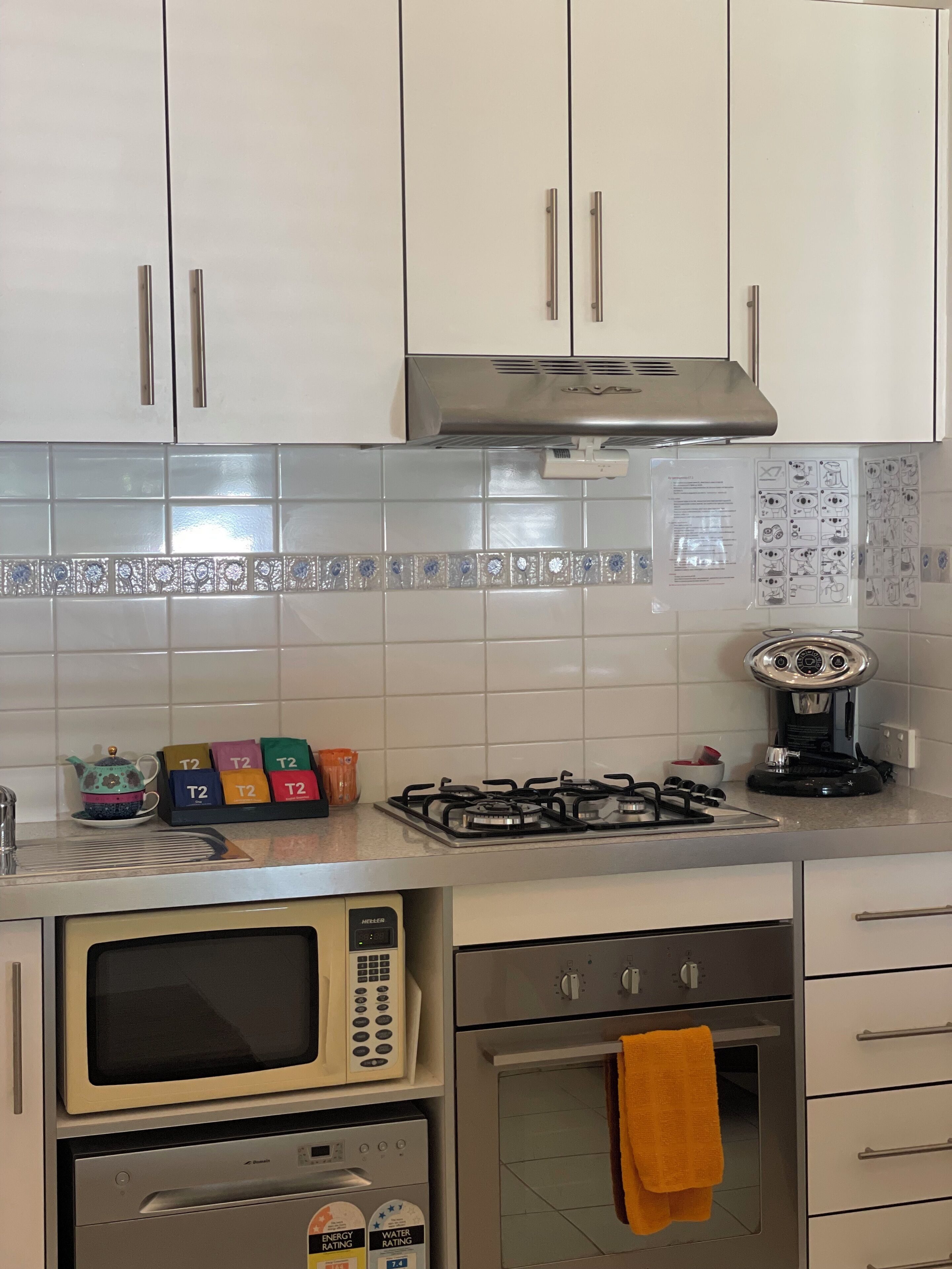 A kitchen with white cabinets, a gas stove, a microwave, an oven, and a kettle.