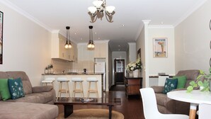 A modern living room with a sofa, a coffee table, and a dining area with a white table and chairs. - CocknBull Boutique Hotel (Echuca)